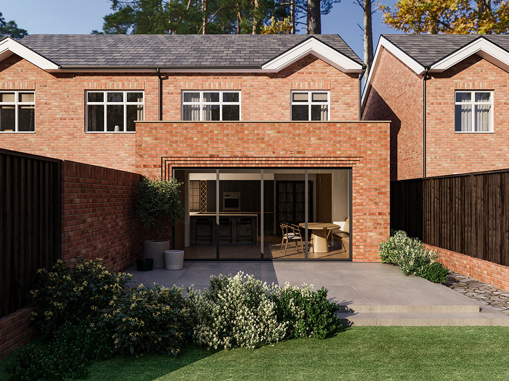 Exterior view of a house extension with a red brick facade and large glass bi-fold patio doors. The extension is attached to an existing two-storey house with matching red bricks. The patio area features plants and a neatly maintained garden.