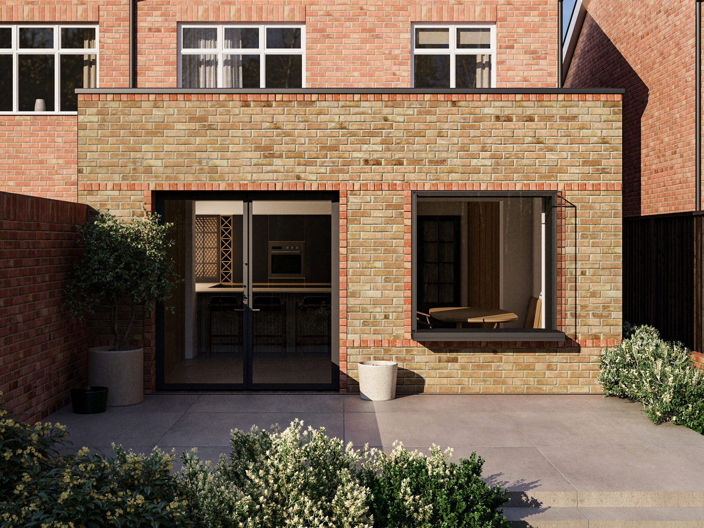 A modern two-storey house with an extended single-storey section in the back garden. The extension features a French-style folding door and an extruded box window. The extension is beige with red detailing, while the rest of the house is red brick. The back garden has a paved patio, steps down to a lawn, bushes, and a wooden fence. Similar houses and trees are visible in the background.