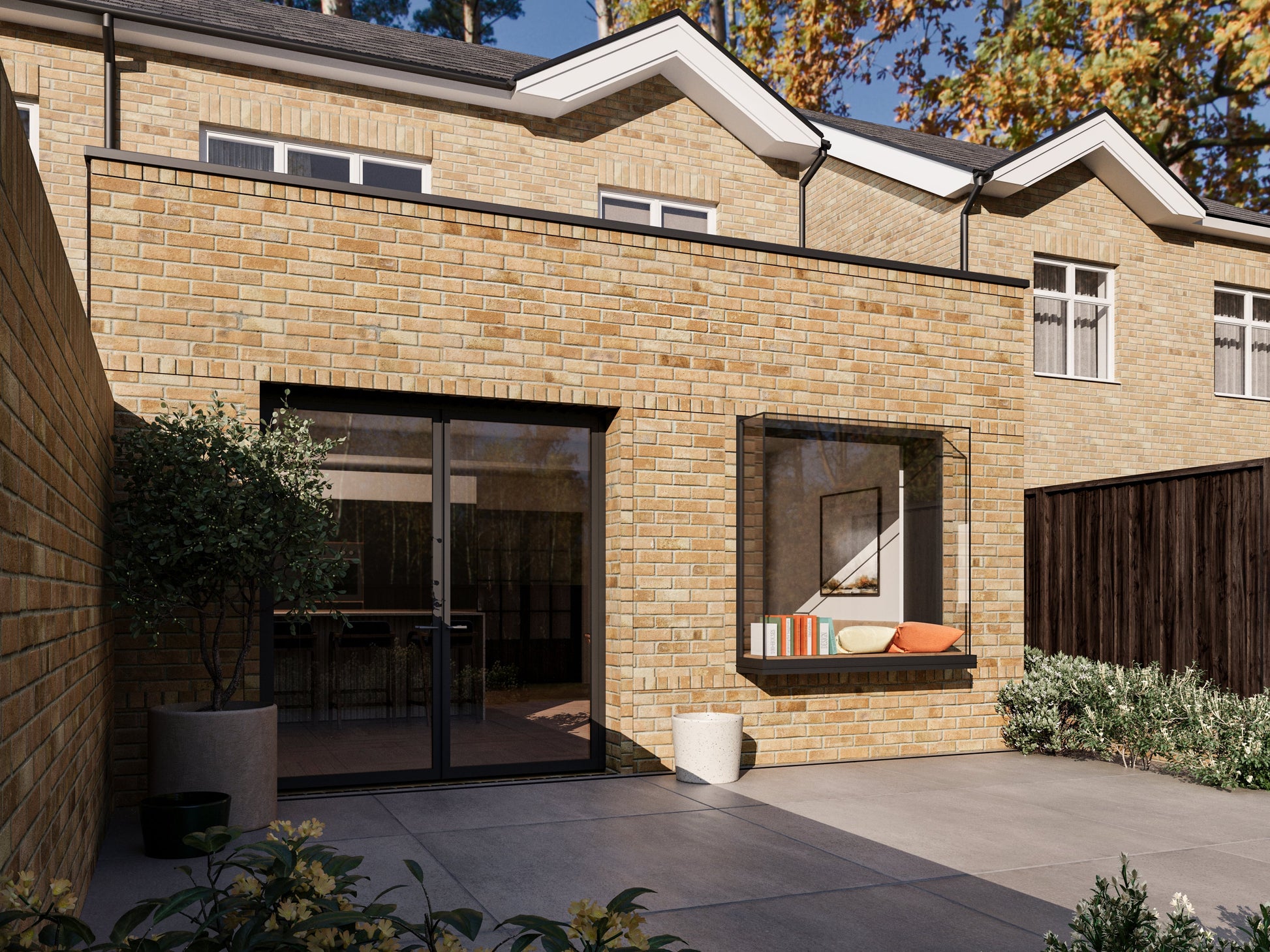 A modern two-storey house with an extended single-storey section in the back garden. The house features large windows, a French-style folding door, and an extruded box window. The extension is yellow brick, while the rest of the house is red brick. The back garden has a paved patio, steps down to a lawn, bushes, and a wooden fence. Similar houses and trees are visible in the background.